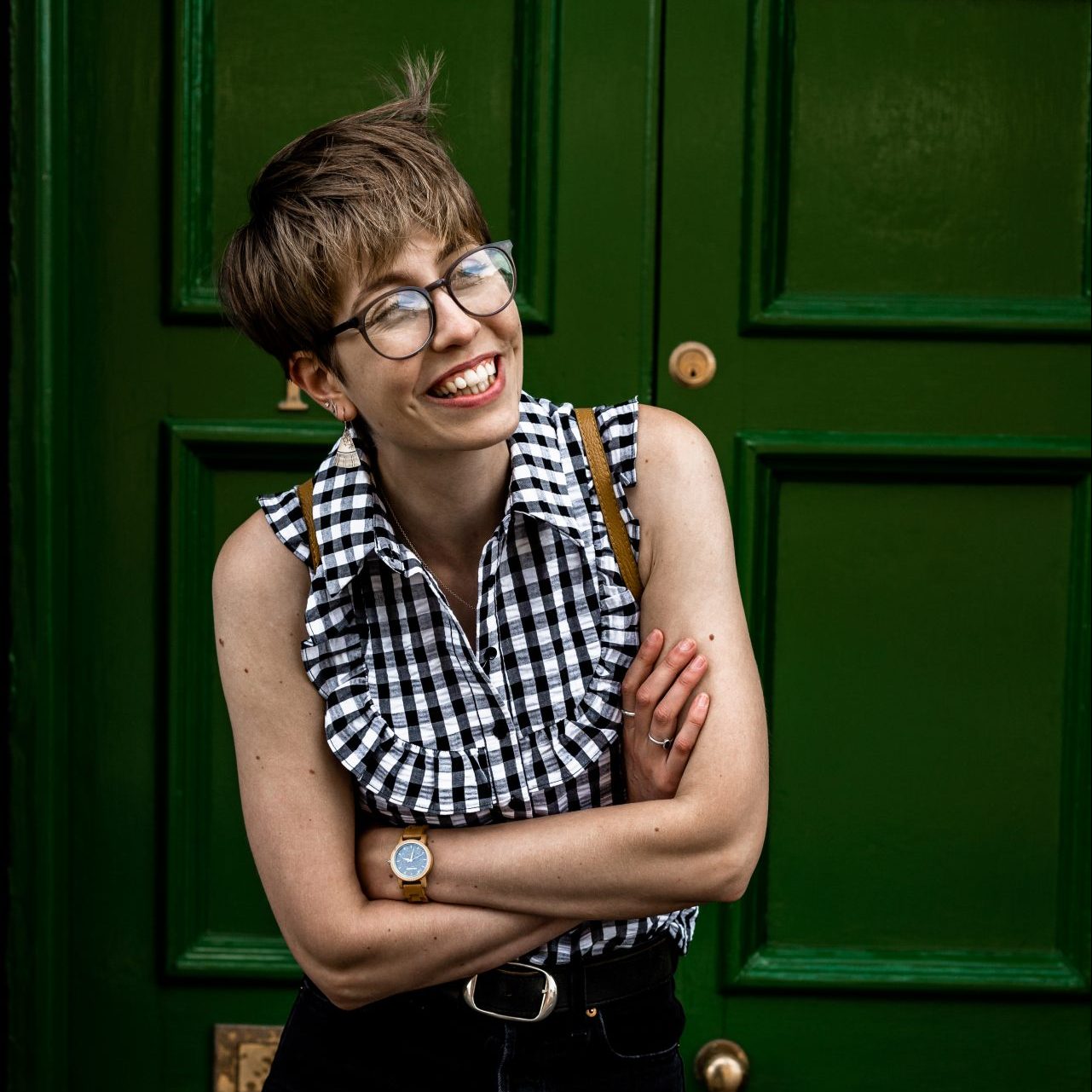 Portrait of Isabelle Biggs Photography shown smiling in front of a green door with her albums crossed