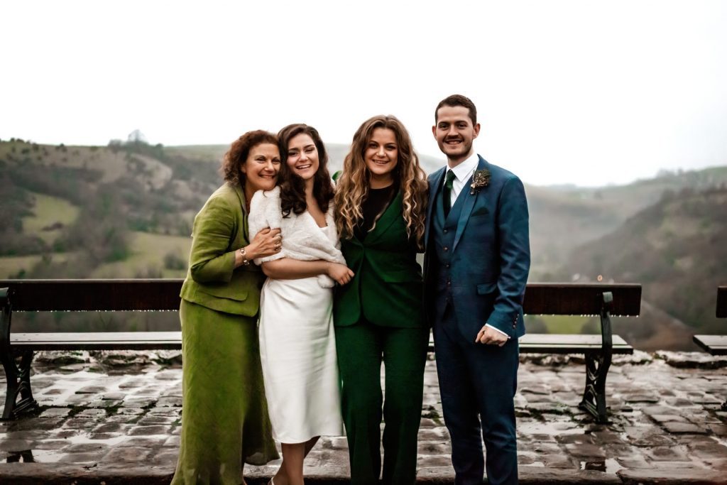 Newly married Bride and Groom photograhed with mother of the bride and sister of the bride at Monsall Head Pub. Bride is wearing a white three-quarter length dress and faux-fur shawl. Groom is wearing a blue three-piece suit and dried flower button-hole. Photo in colour