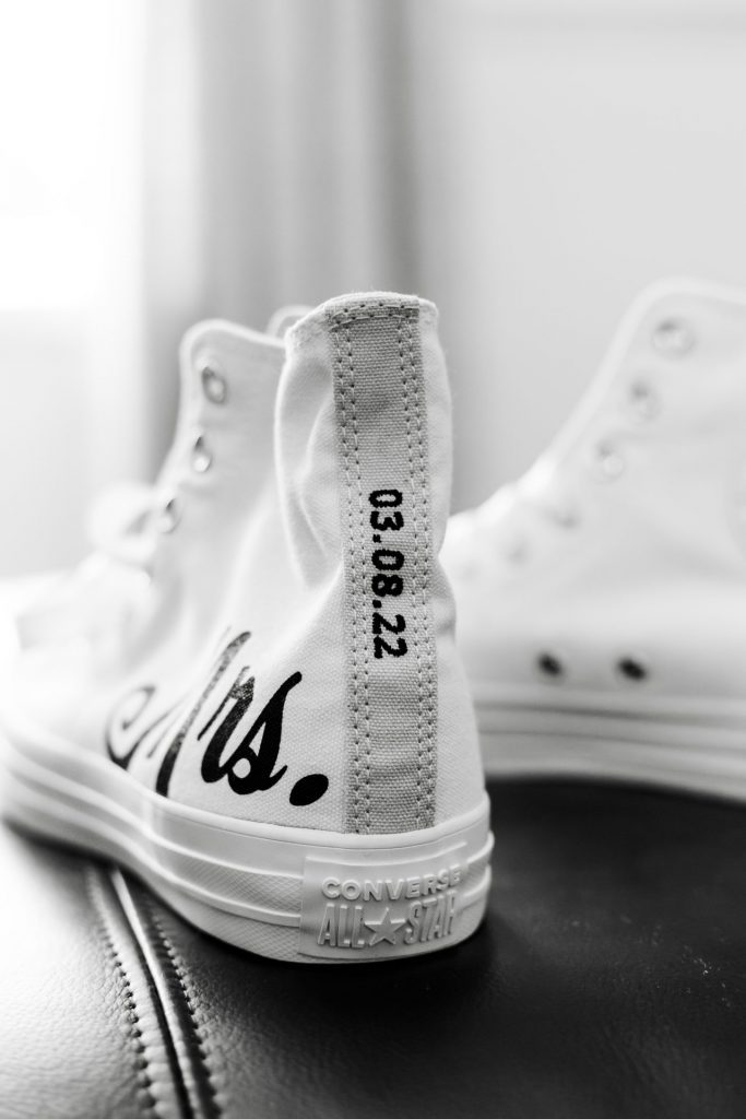 Close-up of the bride's wedding shoes. They are white Converse with the wedding date stitched on the back. Shot during the bridal prep
