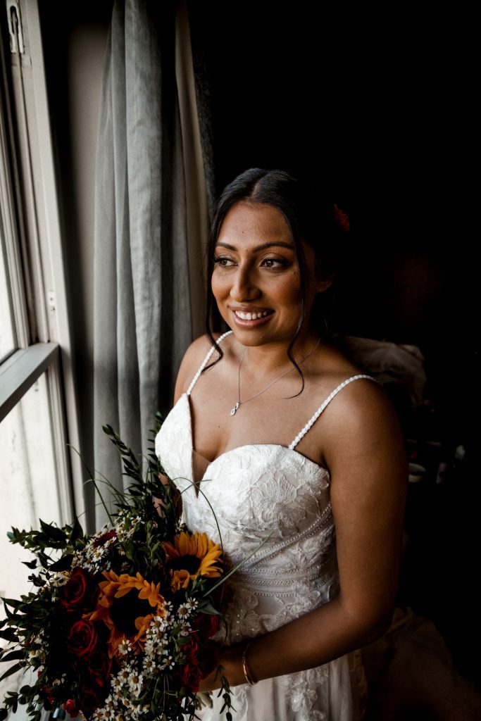 The bride posed in her wedding dress with her bridal bouquet next to the window