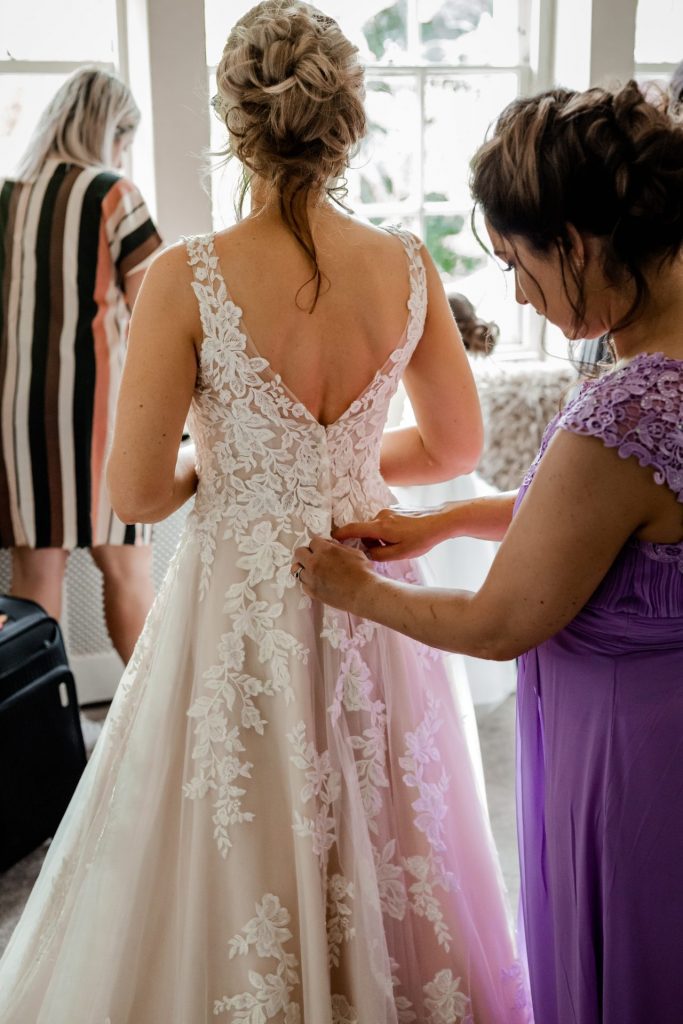 Bridesmaid buttoning up the lace wedding dress