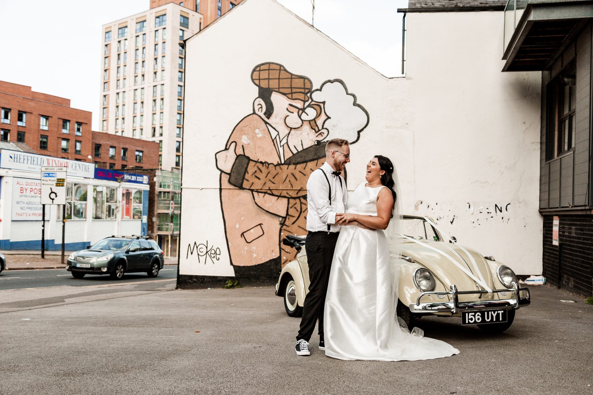Bride & Groom stand in front Pete Mckee mural in Sheffield with a vintage green VW beetle - Alternative Wedding Photographer