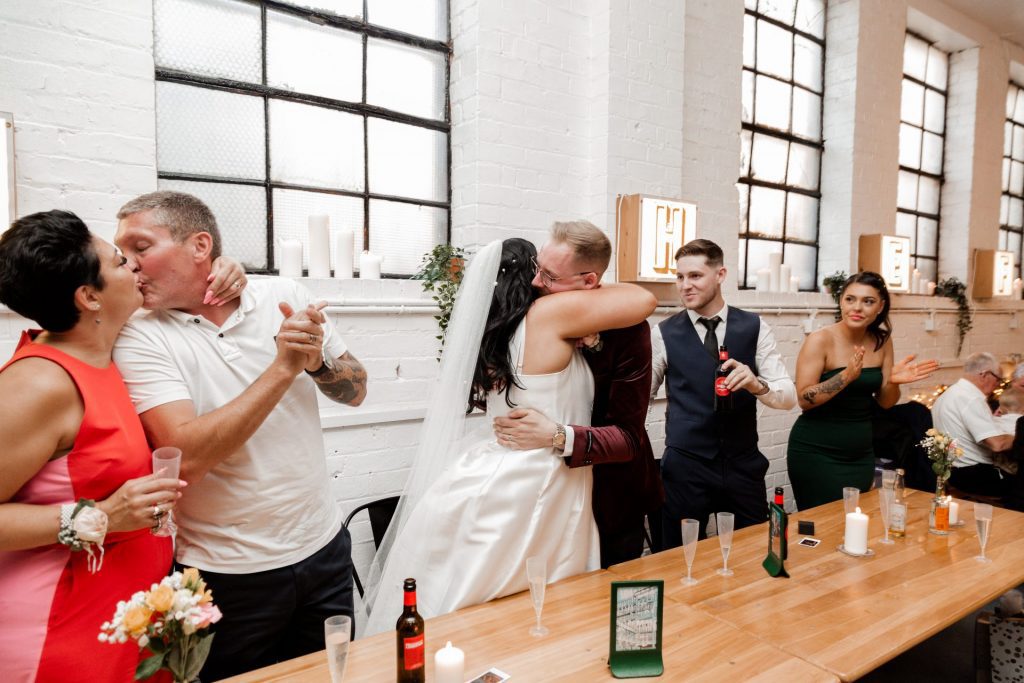 Showing the top table at a wedding. The bride and groom embrace whilst the brides parents share a kiss