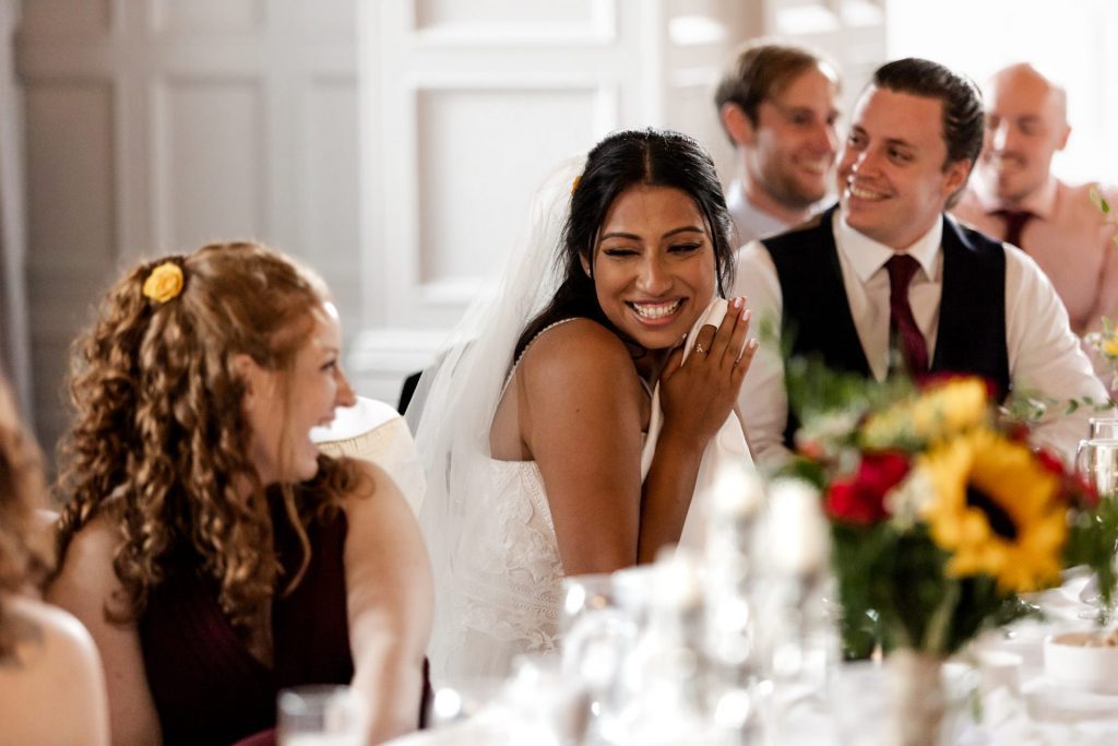 Close up of the bride smiling with her bridesmaid during the father of the bride speech