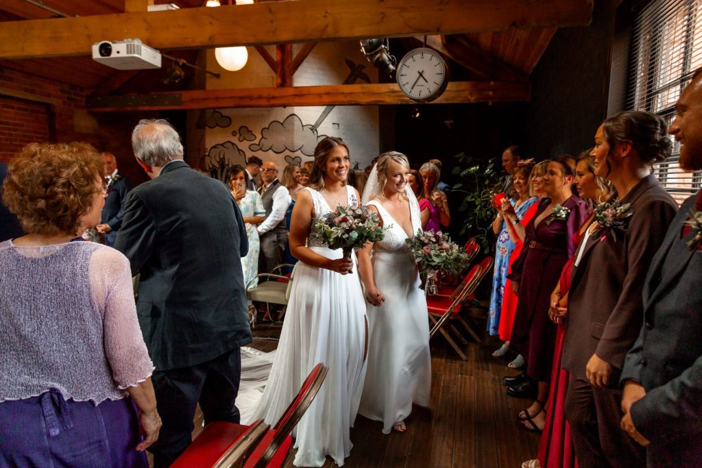 The bride & bride walking hand in hand down the aisle after their wedding ceremony at The Chimney House wedding venue, Kelham Island, Sheffield. Isabelle B Photography