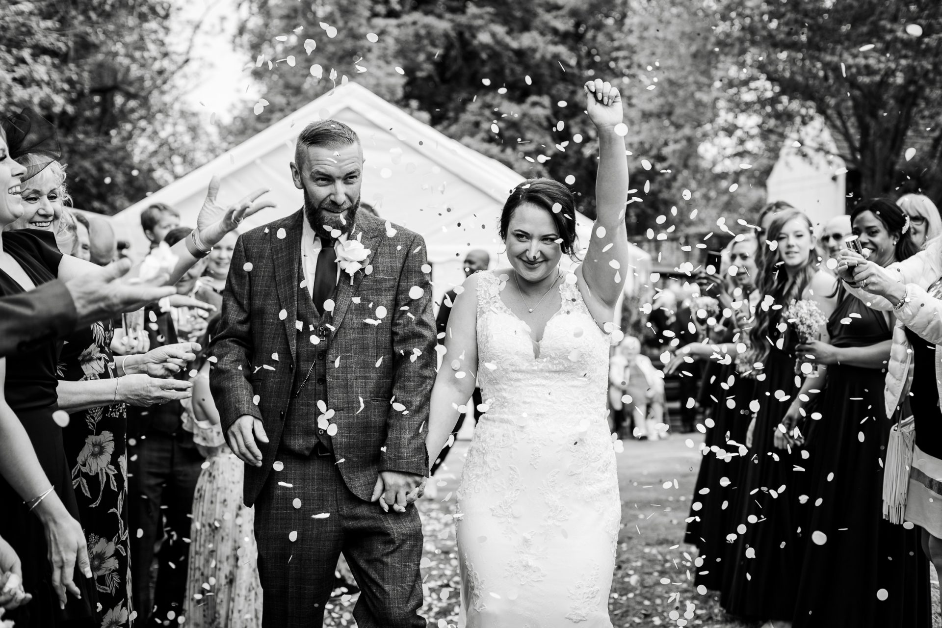 Newly married Bride & Groom walk through their confetti tunnel. The bride is waving her hand in the air. Isabelle B Photography, Sheffield Wedding Photography