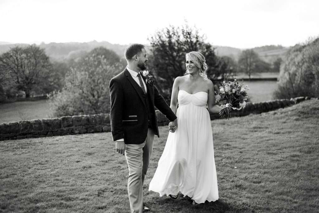 Newly married husband and wife walking together outside their wedding venue, The Cavendish Hotel, Baslow. Black & White