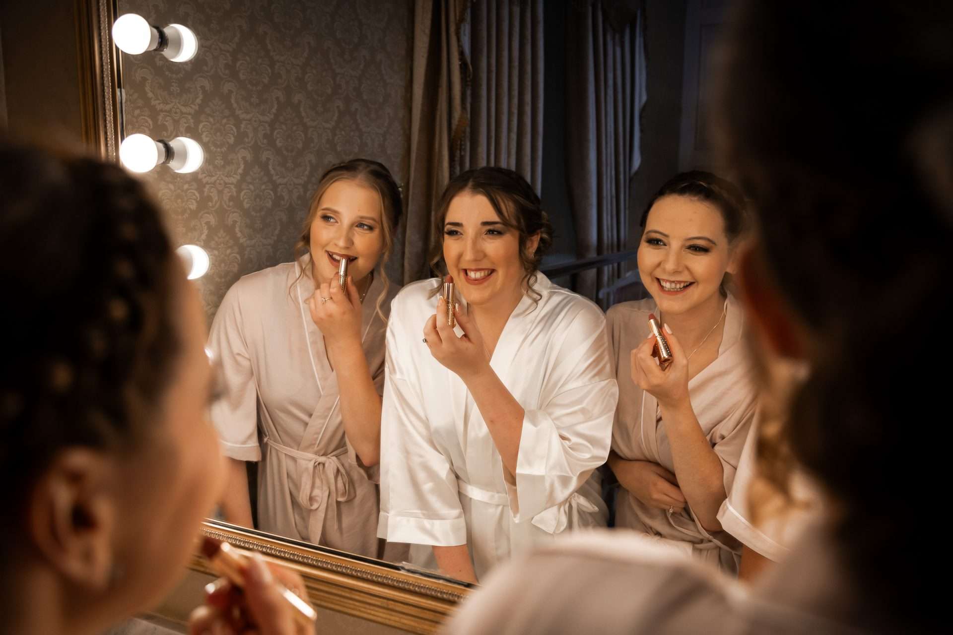 The bride and her bridesmaids applying lipstick in the mirror at Rossington Hall, Doncaster. Isabelle B Photography 