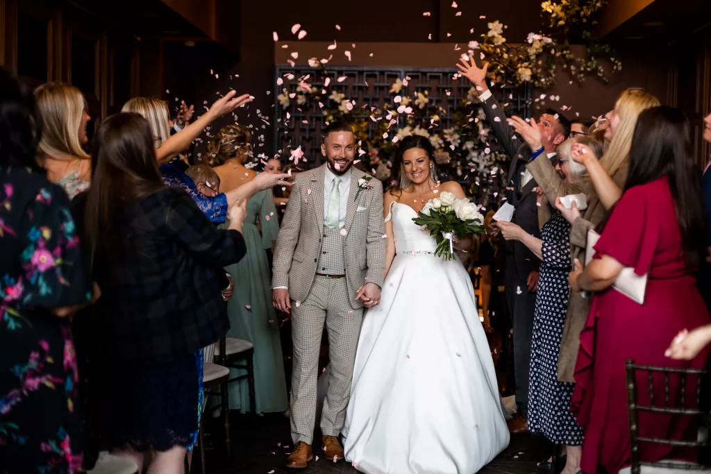 Bride and groom walking pack up the aisle and confetti is being thrown. Inside the ceremony room at the Manor House, Lindley.