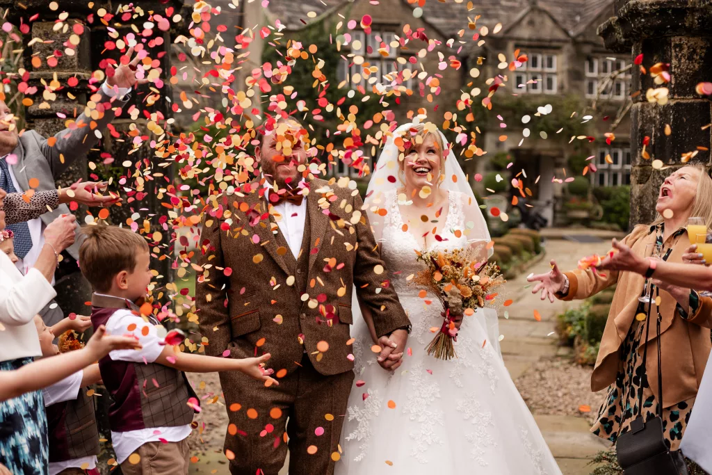 Newly married bride & groom walking through their confetti tunnel. The confetti is bright orange, red & yellow Flutter Darlings confetti
