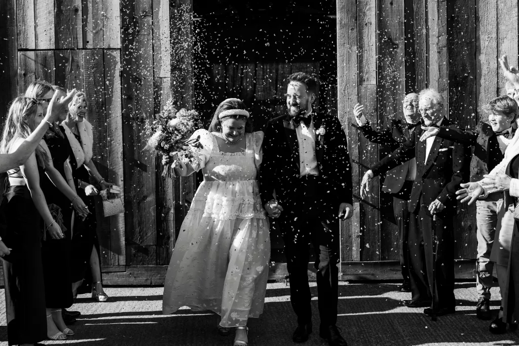 Newly married bride & groom walking through their confetti tunnel - black and white