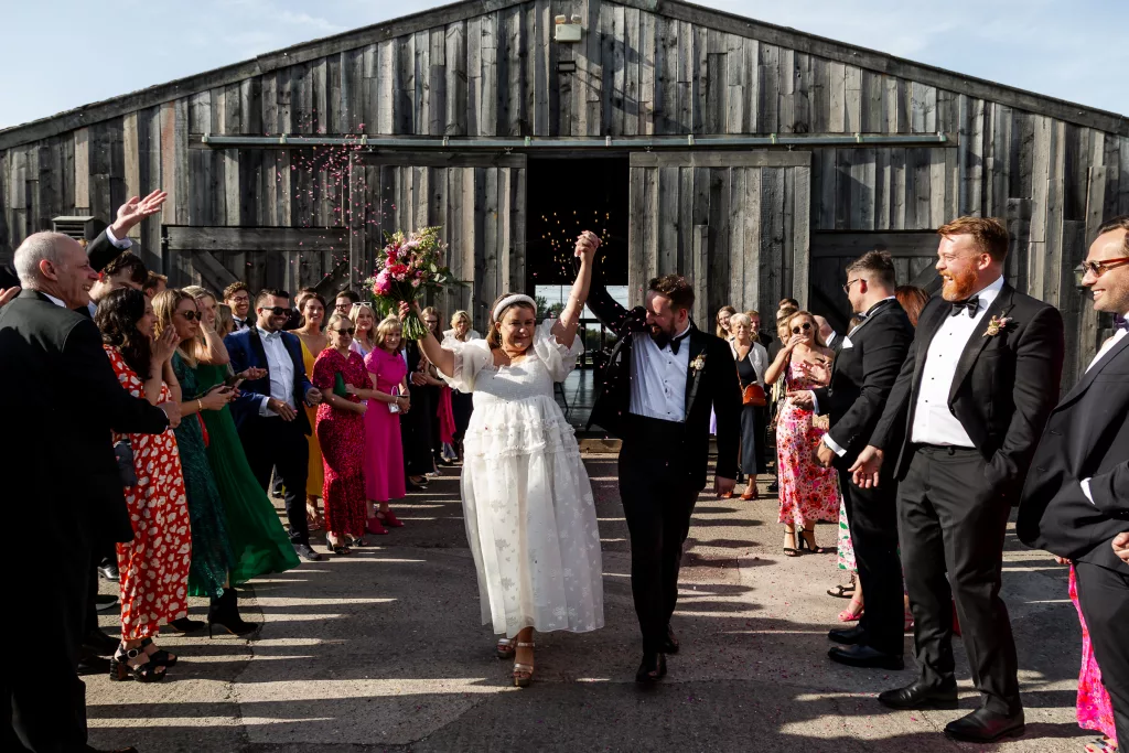 Newly married bride & groom walking through their confetti tunnel with their hands in the air