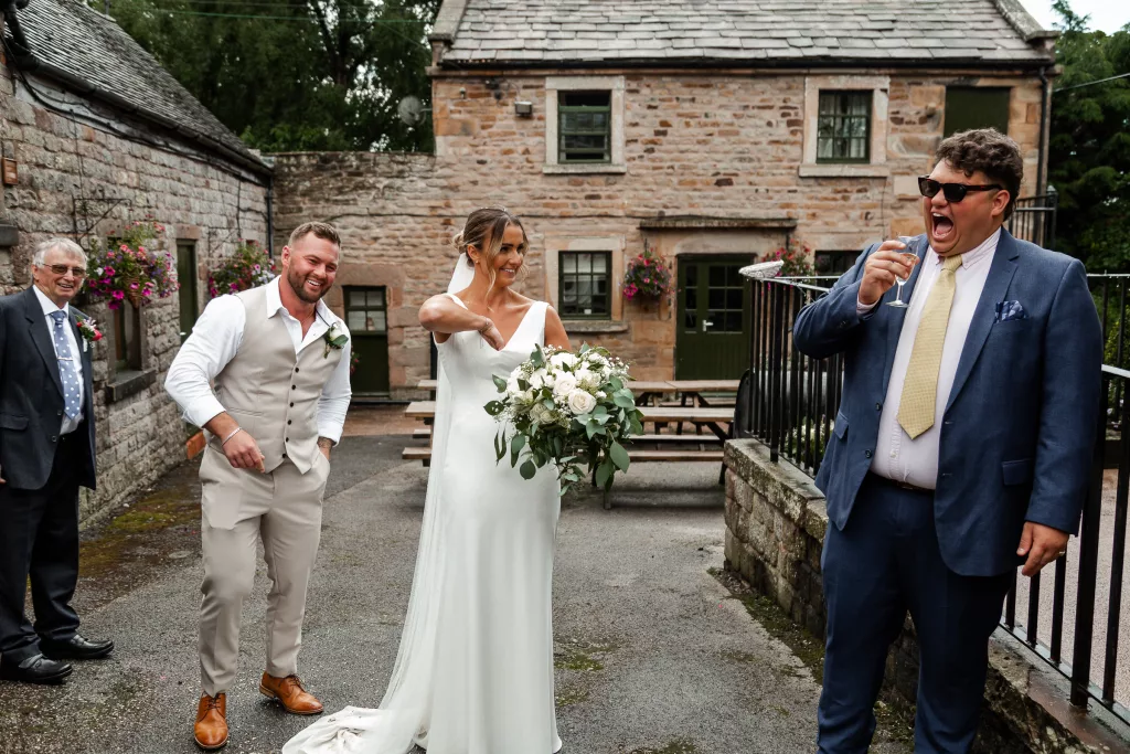 The bride reaching down her top to grab confetti after the confetti tunnel. One of the guests is laughing loudly at the sight