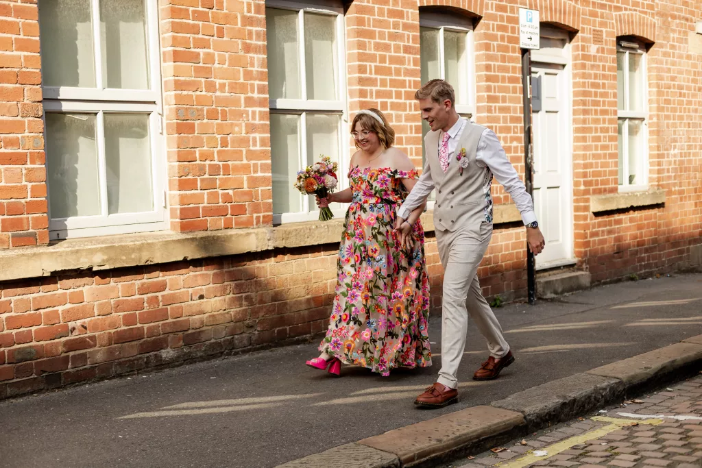 Newly married husband and wife walking together. The bride is wearing a colourful flower embroidered dress and groom is wearing a light coloured suit with a pink tie to match the brides dress