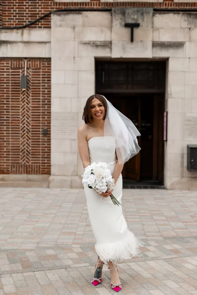 The bride stood outside of their wedding venue, The Tetley, Leeds. The bride an alternative three quarter length wedding dress with pink heels and a short veil