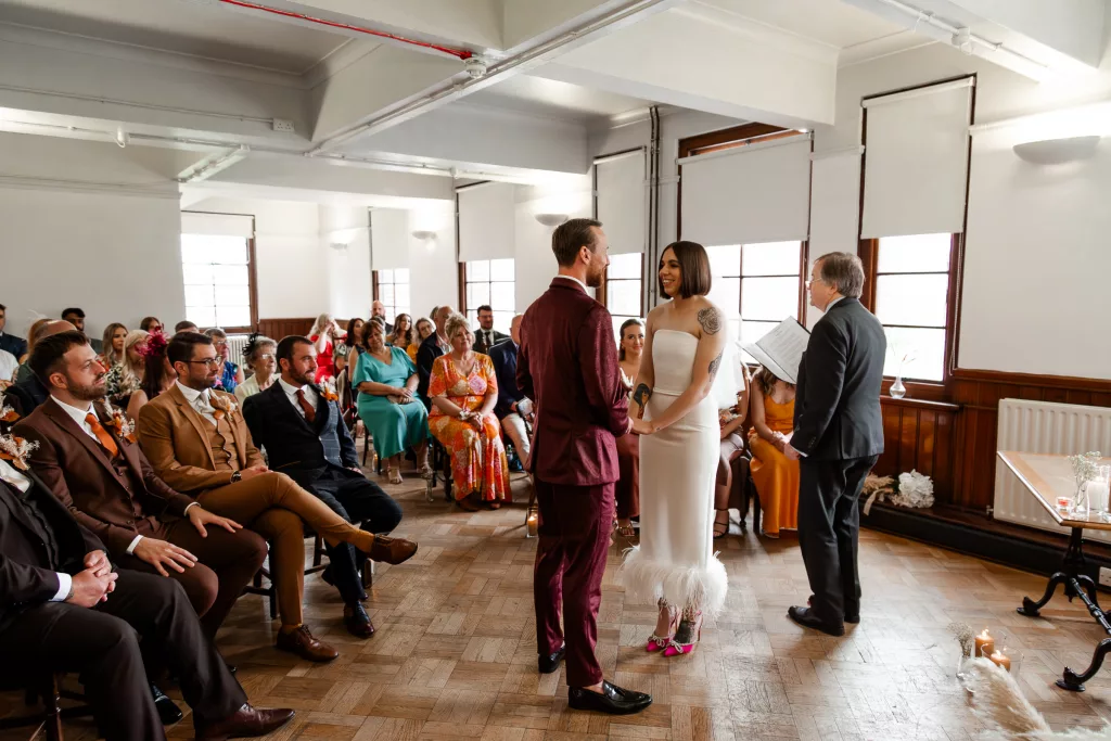 The bride & groom stood together during their wedding ceremony at The Tetley, Leeds. The groom wearing a purple velvet suit, and the bride an alternative three quarter length wedding dress