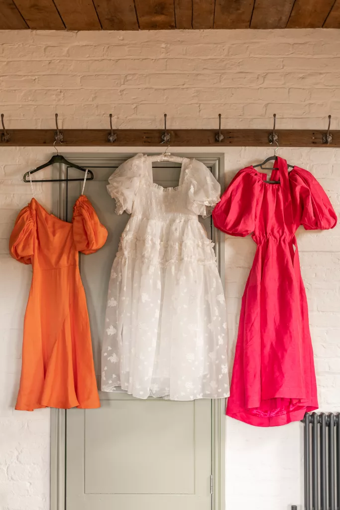 A shot of a alternative wedding dress hanging next to 2 bridesmaids dresses. One in pink, one in orange. At the Grange Barn, Cheshire.