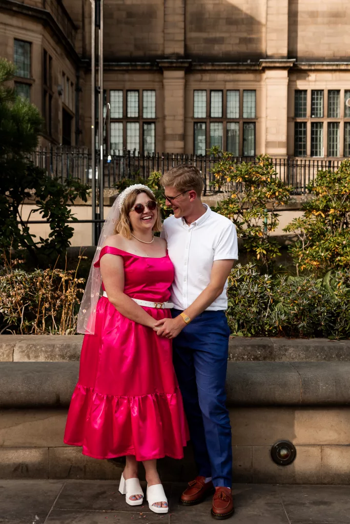 Newly married bride & groom stood together outside Sheffield Town Hall. The bride is wearing an alternative bright pink wedding dress