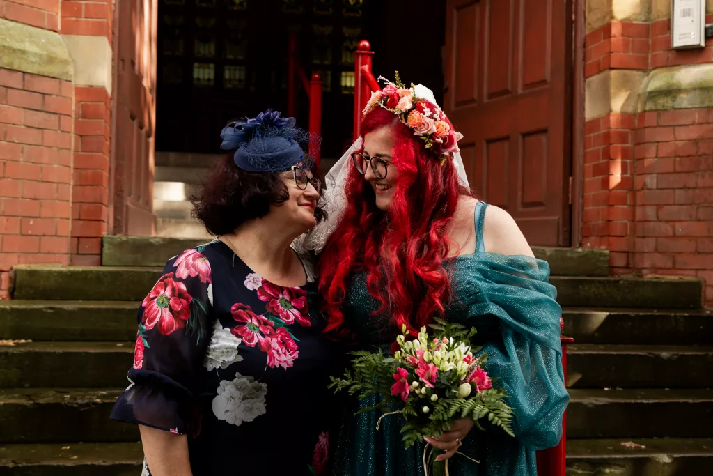 Bride and mother of the bride stood together outside Dukenfield town hall after their wedding ceremony. The bride wearing an alternative vibrant blue wedding dress