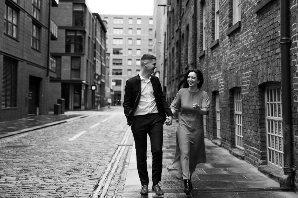 Newly engaged couple walking together in Ancoats, Manchester - The bride to-be is wearing a vivid red dress & the groom to-be is wearing a blue suit - Engagement Shoot - Isabelle B Photography