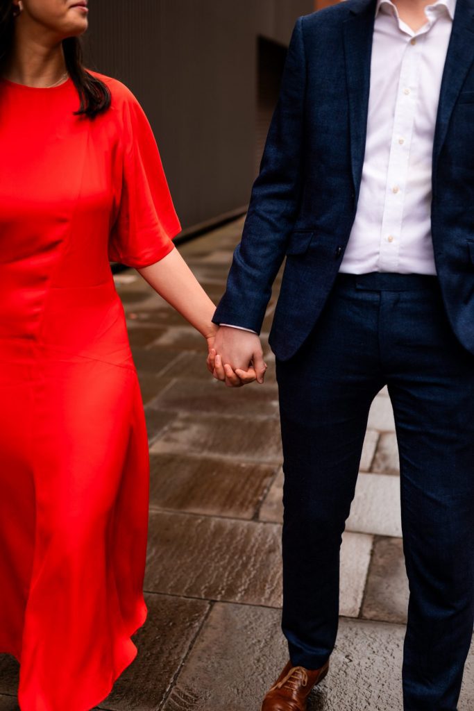 Newly engaged couple walking together in Ancoats, Manchester - The bride to-be is wearing a vivid red dress & the groom to-be is wearing a blue suit - Engagement Shoot - Isabelle B Photography