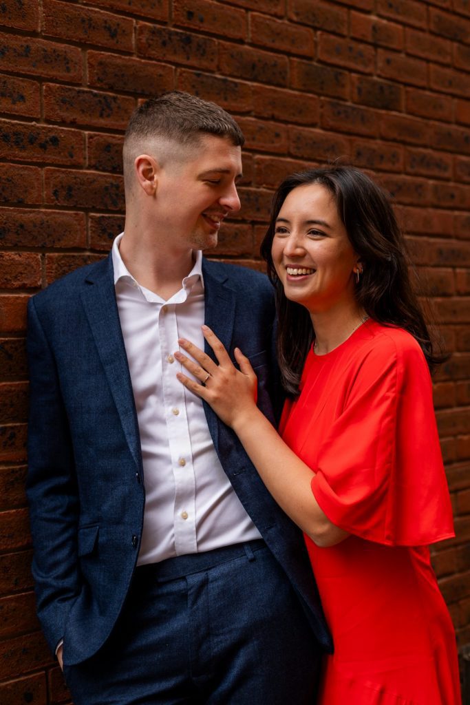 Newly engaged couple walking together in Ancoats, Manchester - The bride to-be is wearing a vivid red dress & the groom to-be is wearing a blue suit - Engagement Shoot - Isabelle B Photography