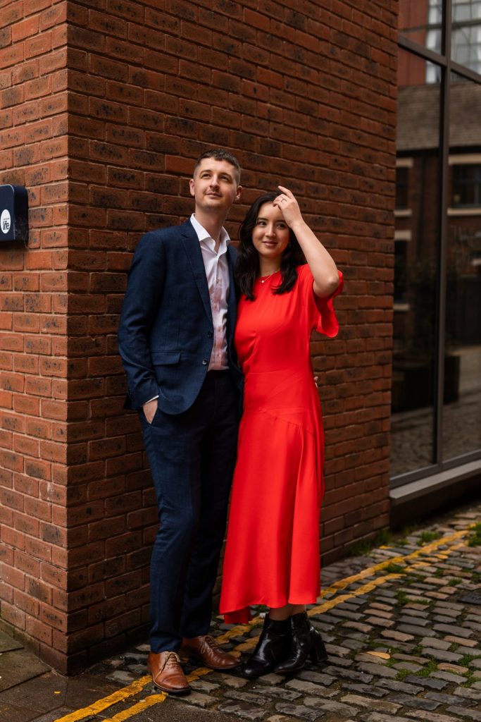 Newly engaged couple walking together in Ancoats, Manchester - The bride to-be is wearing a vivid red dress & the groom to-be is wearing a blue suit - Engagement Shoot - Isabelle B Photography