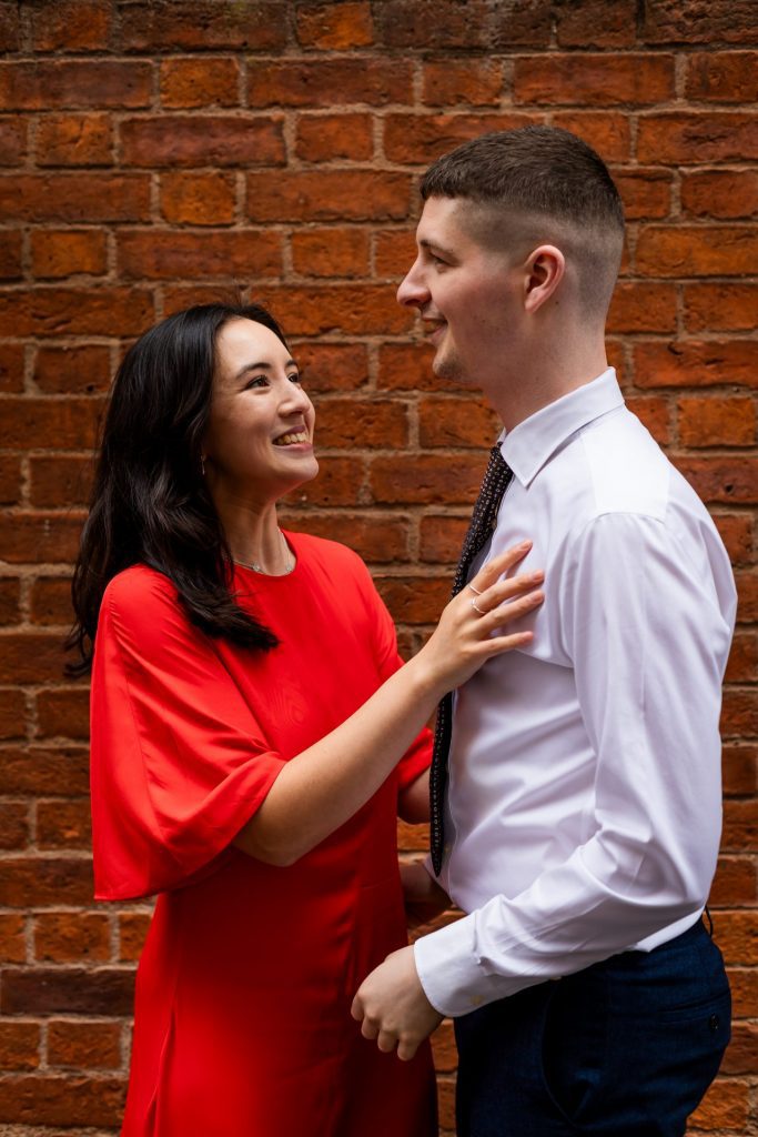 Newly engaged couple walking together in Ancoats, Manchester - The bride to-be is wearing a vivid red dress & the groom to-be is wearing a blue suit - Engagement Shoot - Isabelle B Photography